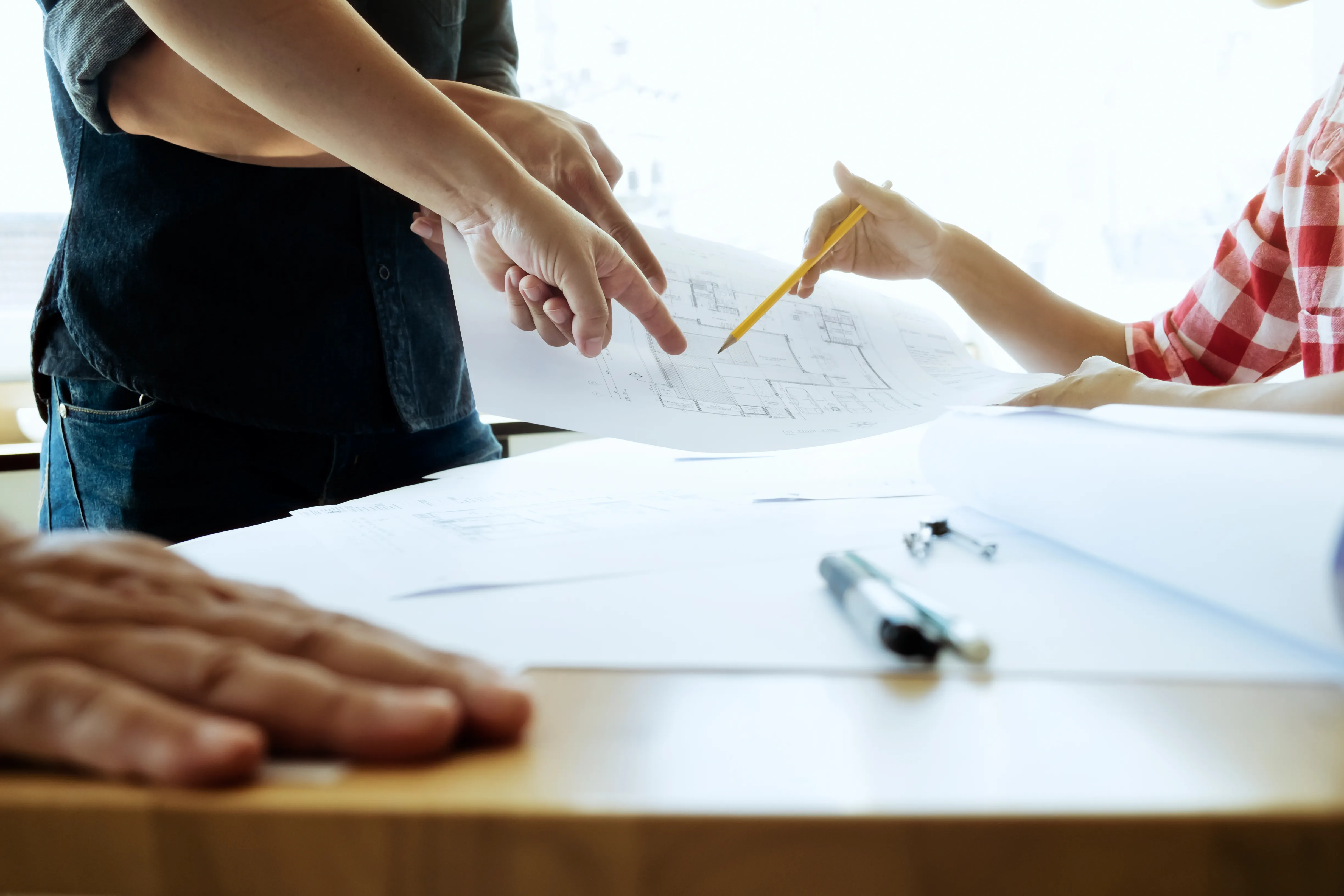 Personen analysieren Baupläne auf einem Tisch mit mehreren Zeichnungen und Bürobedarf