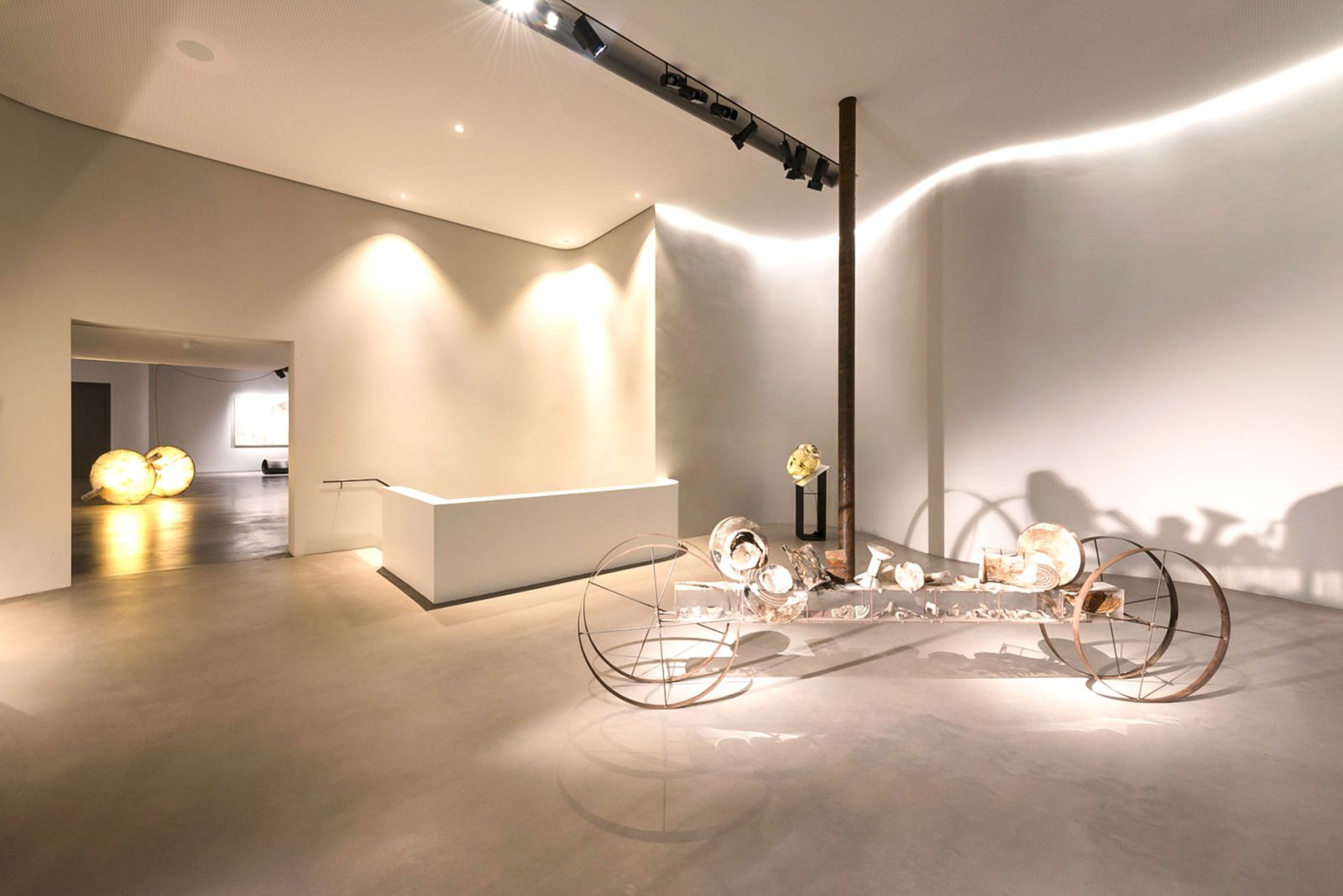 Heller Ausstellungsraum mit modernen Kunstinstallationen und geschwungener Wandbeleuchtung