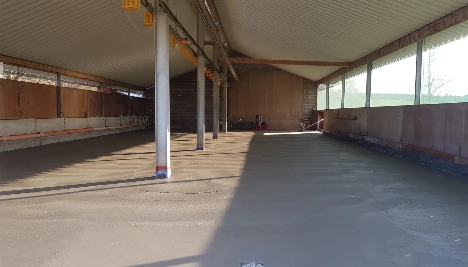 Betonierarbeiten in einer langen, offenen Halle mit Metall- und Holzkonstruktion