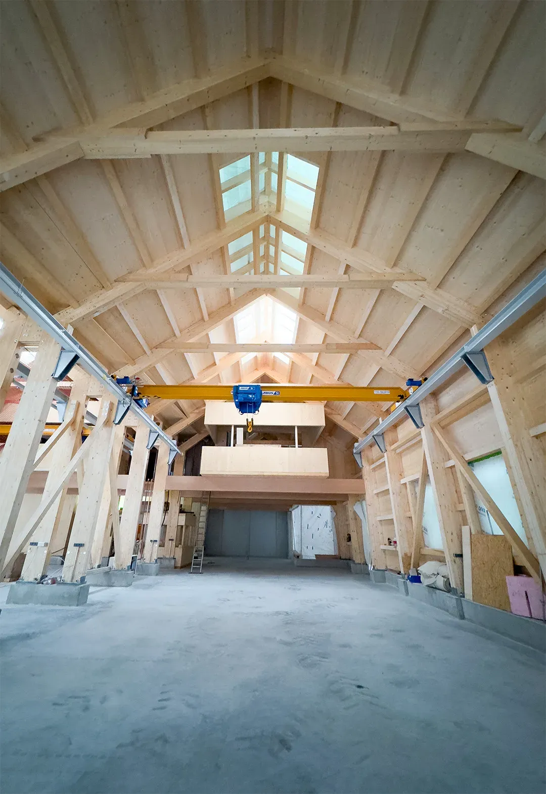 Innenansicht einer Holzhalle mit Krananlage und Dachfenstern