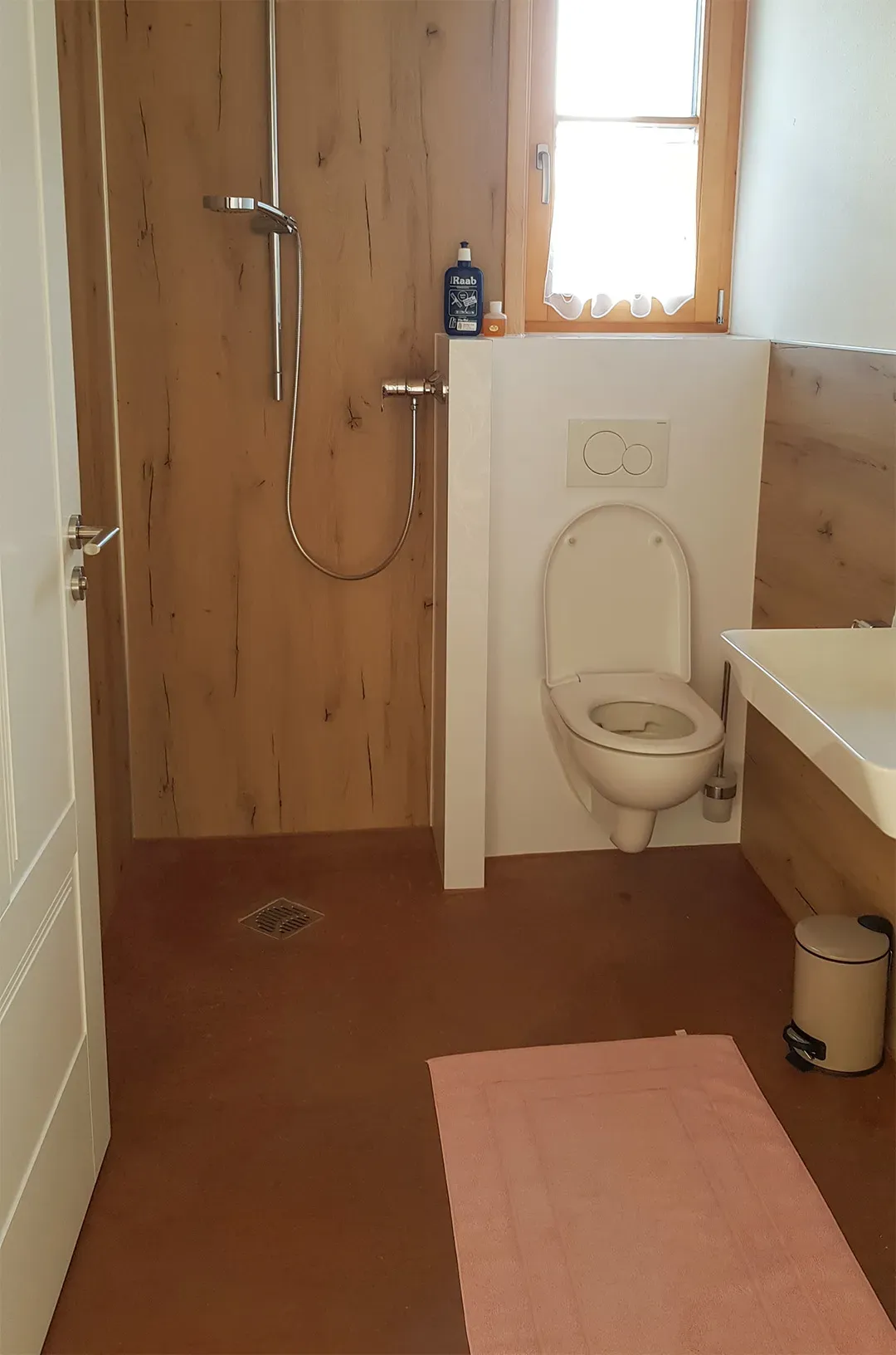 Badezimmer mit Holzwänden, einer offenen Dusche, einem Hänge-WC und rötlichem Boden