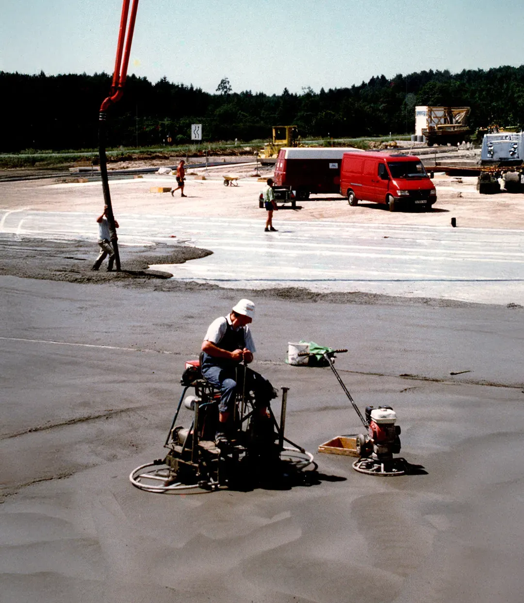 Baustelle mit Arbeiter auf einer Beton-Glättmaschine, frisch nivellierter Betonboden im Vordergrund