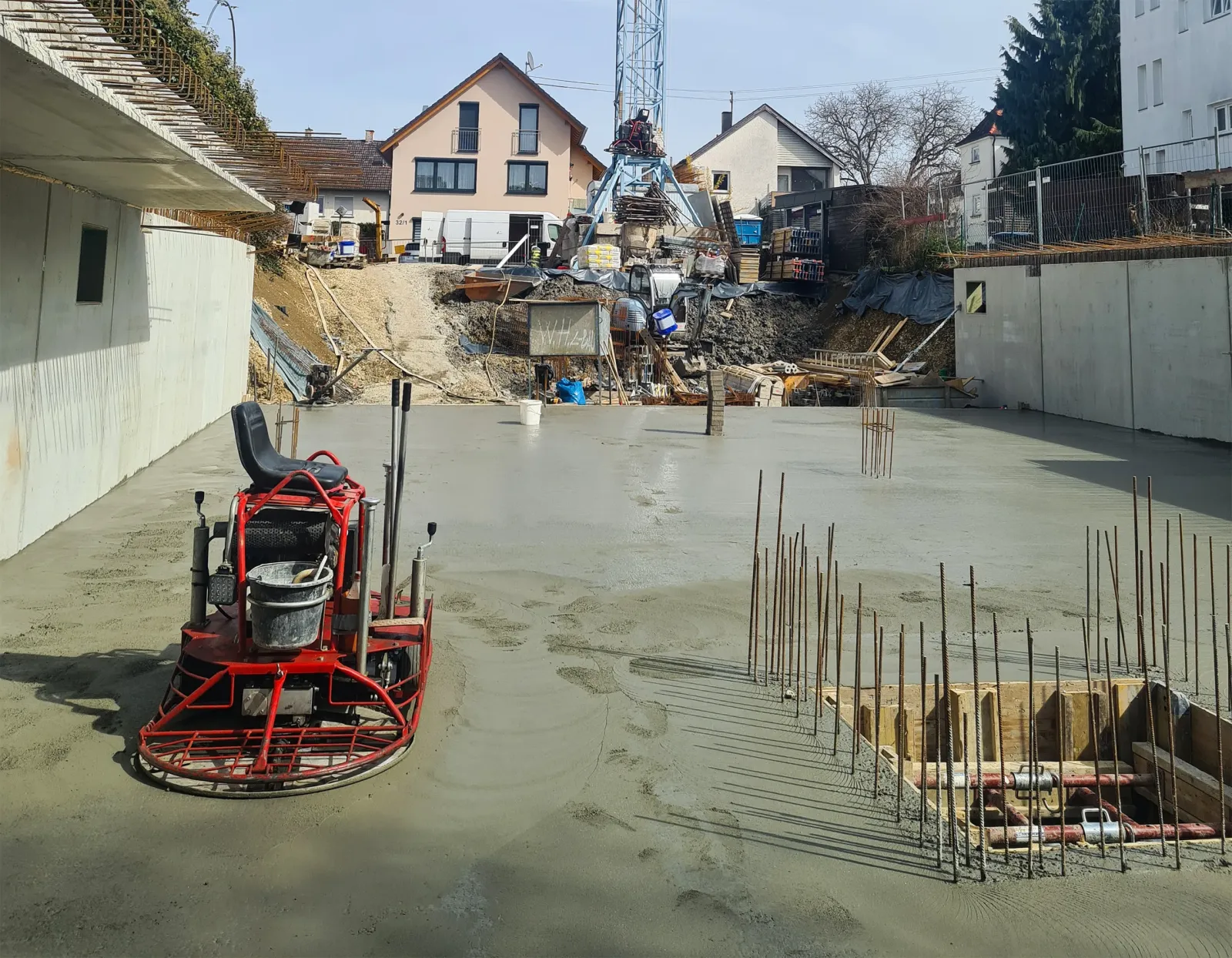 Baustelle eines Kellerfundaments mit frischem Estrich, Beton-Glättmaschine und sichtbaren Baustahlmatten