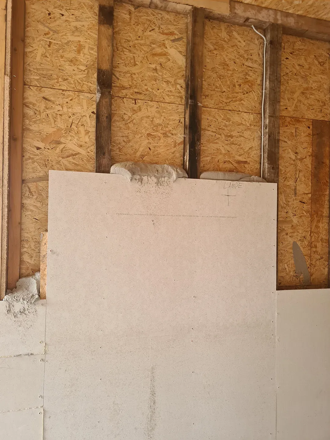 Holzwandkonstruktion mit OSB-Platten, Dämmstoff in Lücken eingebracht und Beschriftung für die Position einer Lampe