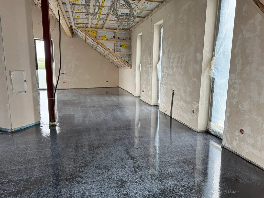 Neubauinnenbereich mit frisch appliziertem, glänzendem schwarzen Bodenbelag und Sicht auf die Dachkonstruktion