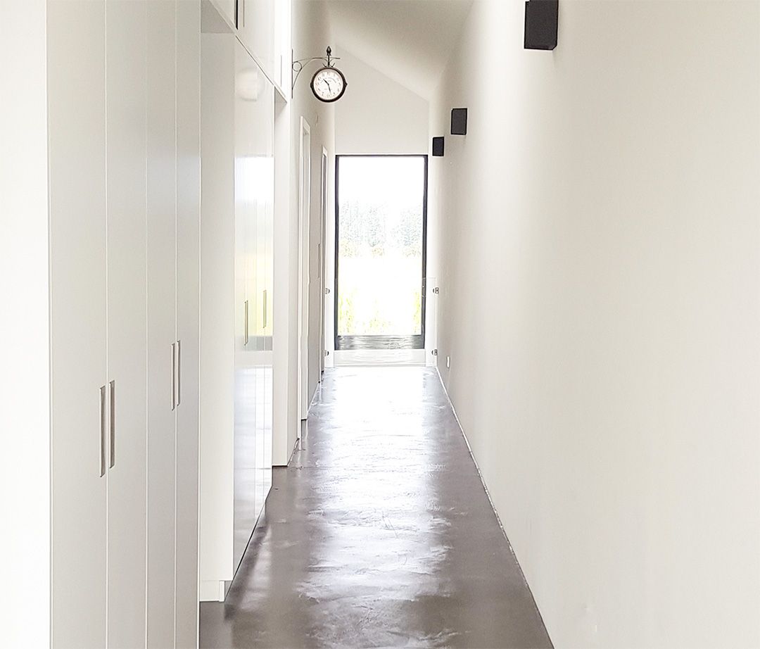 Minimalistischer, lichtdurchfluteter Flur mit weißen Einbauschränken, einer Wanduhr und Blick auf die Glasaußentür