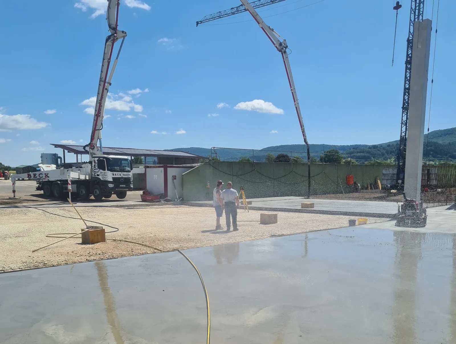 Großbaustelle im Freien mit Betonpumpen und Baumaschinen, frisch gegossene Betonfläche im Vordergrund