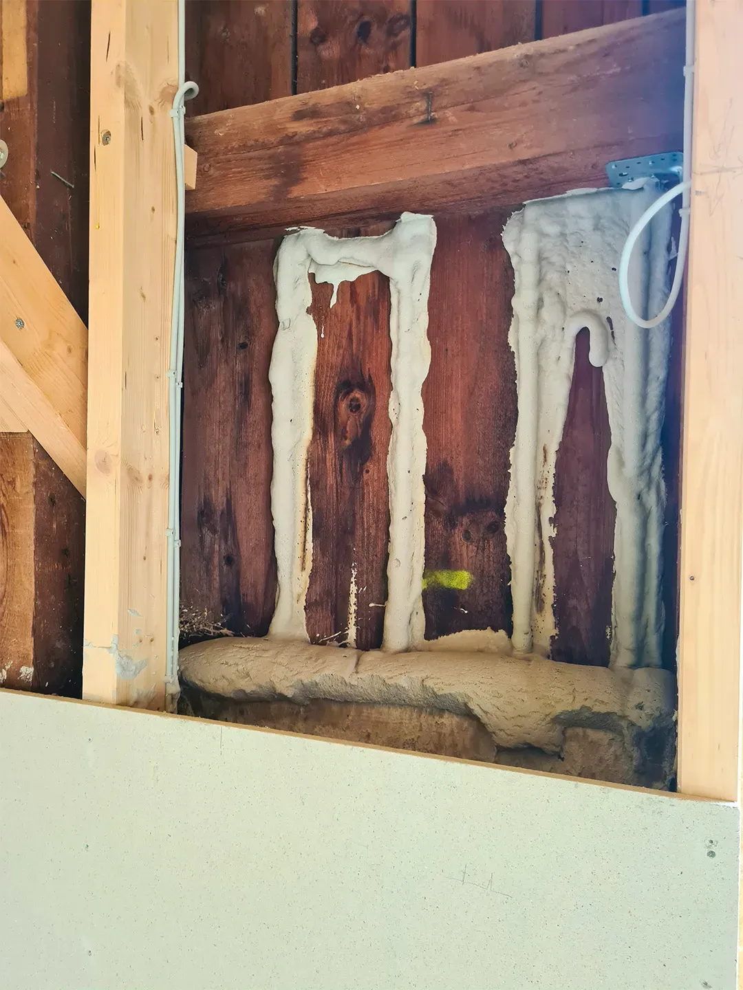 Ausschnitt einer Wandkonstruktion mit offenen Hohlräumen und aufgebrachter Sprühschaumdämmung entlang vertikaler Balken