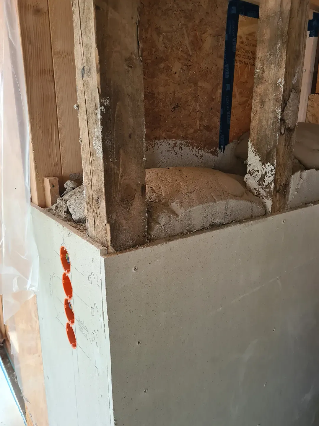 Eckbereich einer Wandkonstruktion mit einsehbaren Holzbalken, teils eingebauter Dämmung und vorbereiteten Elektrodosen