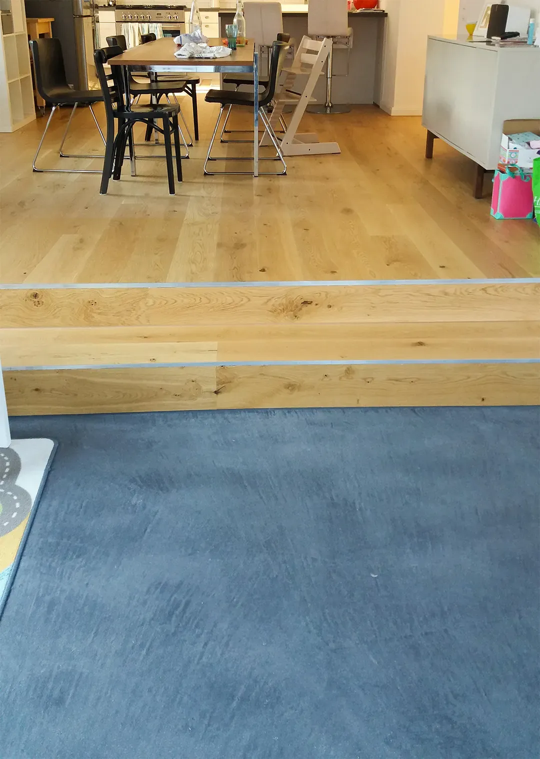 Wohnraum mit dunklem Boden, erhöhtem Essbereich mit hellem Holzboden und moderner Einrichtung